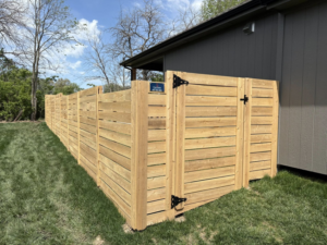 A modern horizontal slat wooden fence with a gate installed next to a house by Fry's Fence LLC in Grain Valley, MO.