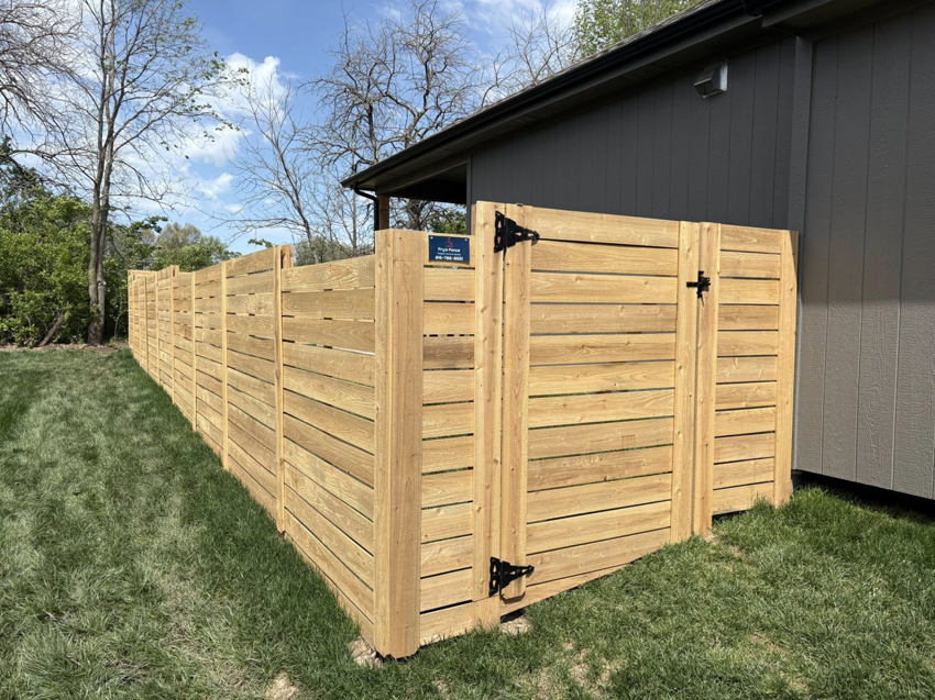 A modern horizontal slat wooden fence with a gate installed next to a house by Fry's Fence LLC in Grain Valley, MO.