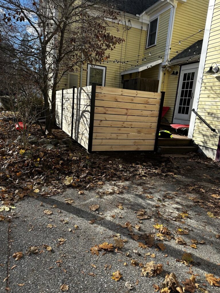 A modern horizontal wood slat fence installed as a privacy screen next to a residential building by New England landscaping and fence inc in Lynn, MA.