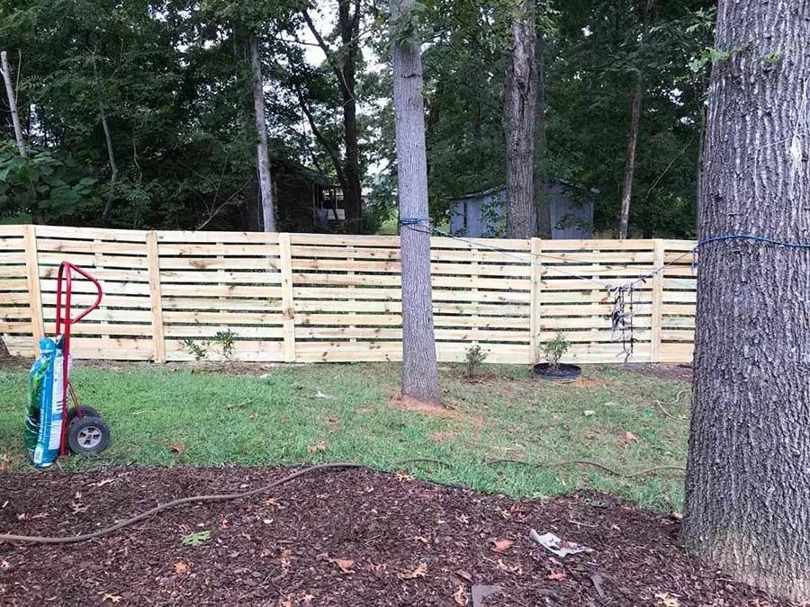 A newly installed horizontal wood slat privacy fence in a wooded backyard by FenceMax in Spartanburg, SC