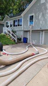 Hoses extending into a house window, likely for attic insulation or pest treatment by KC Pest Experts in Olathe, KS.