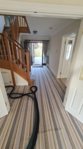 Carpet cleaning hoses laid across a striped carpet in an entrance hall by Plymouth Carpet Cleaners in Hooe, UK.