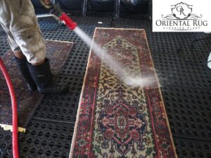 A worker hosing down a small oriental rug as part of the cleaning service at Oriental Rug Cleaning Facility in Tampa, FL