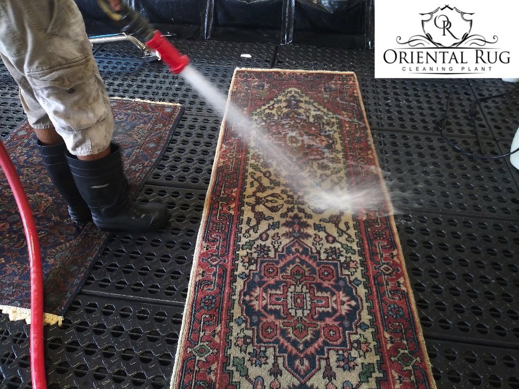 A worker hosing down a small oriental rug as part of the cleaning service at Oriental Rug Cleaning Facility in Tampa, FL