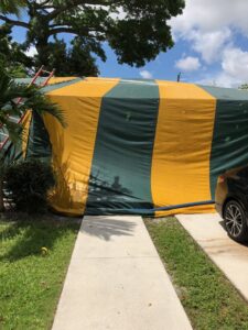 A house completely covered in a yellow and green striped tarp for fumigation by Globe Pest Inc in Miami, FL.