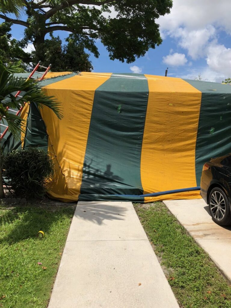 A house completely covered in a yellow and green striped tarp for fumigation by Globe Pest Inc in Miami, FL.