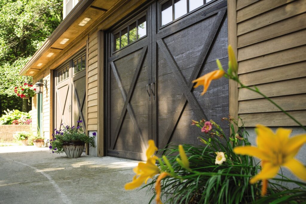 A beautiful home featuring dark brown carriage-style garage doors, enhanced by vibrant flowers, installed by Monroe Overhead Doors in Monroe, LA.