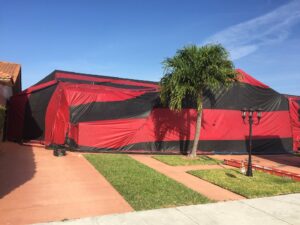 A house covered in a distinctive black and red striped tarp for fumigation by Globe Pest Inc in Miami, FL.