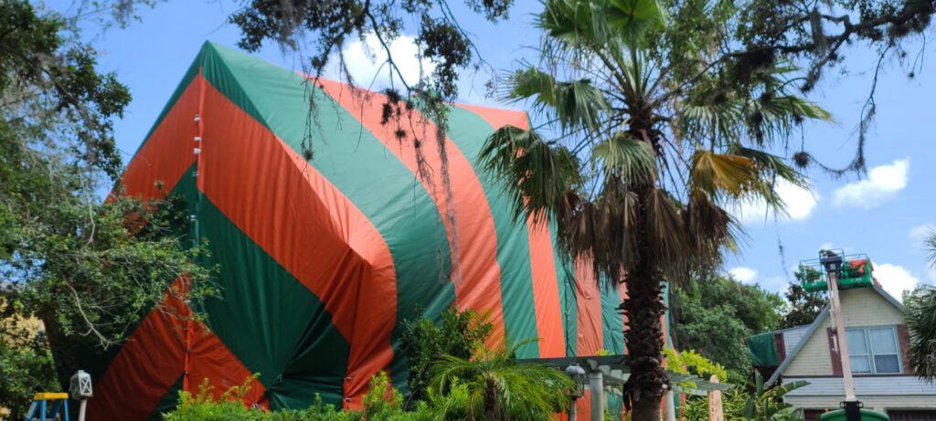 A residential house covered in a red and green fumigation tent, surrounded by trees, by Rivers Pest Control Service, Inc. in Jacksonville, FL