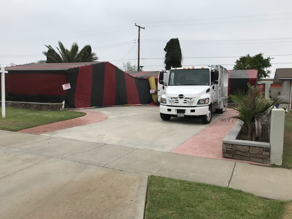 A house covered in red and black fumigation tenting with a service truck parked by Intensive Pest Control in Long Beach, CA.
