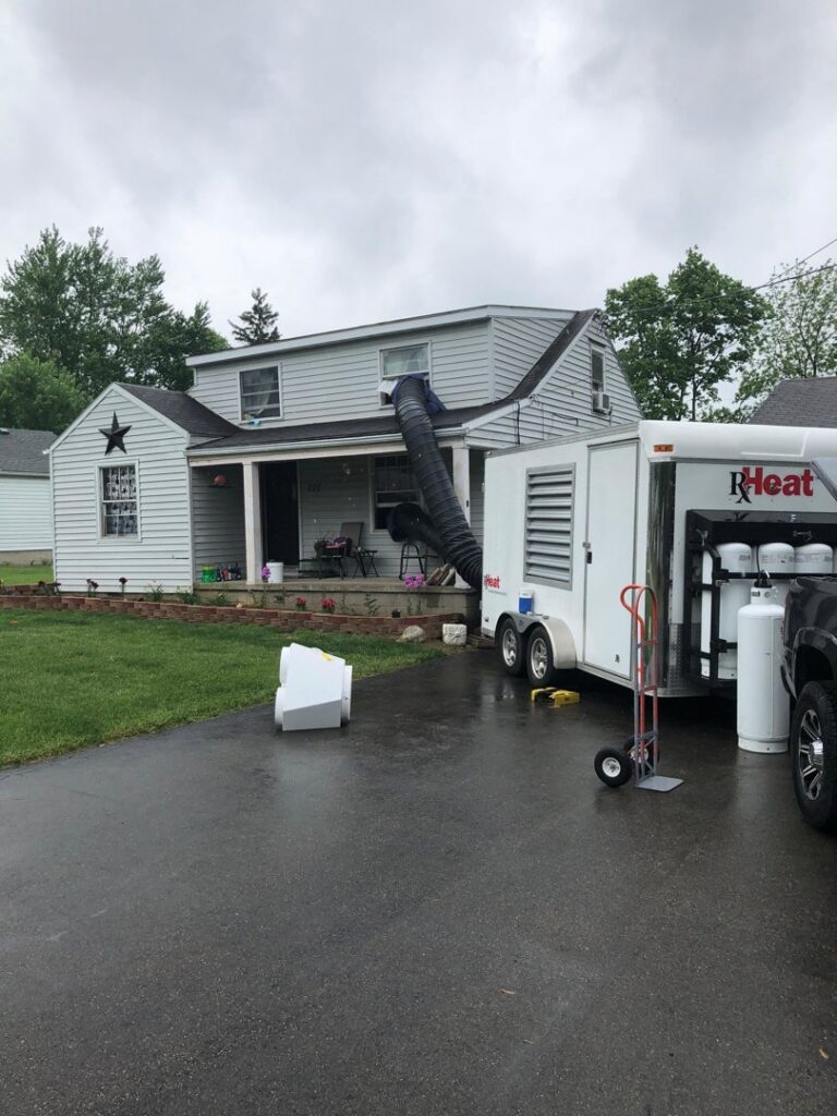 A house receiving a heat treatment for pests, with a large duct extending from a specialized trailer into an upper window, by Bayer Pest Control in Dayton, OH.