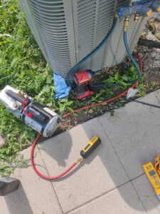 HVAC tools, including a vacuum pump and manifold gauges, connected to an AC system for service by Chief/Bauer Service Experts in Champaign, IL.