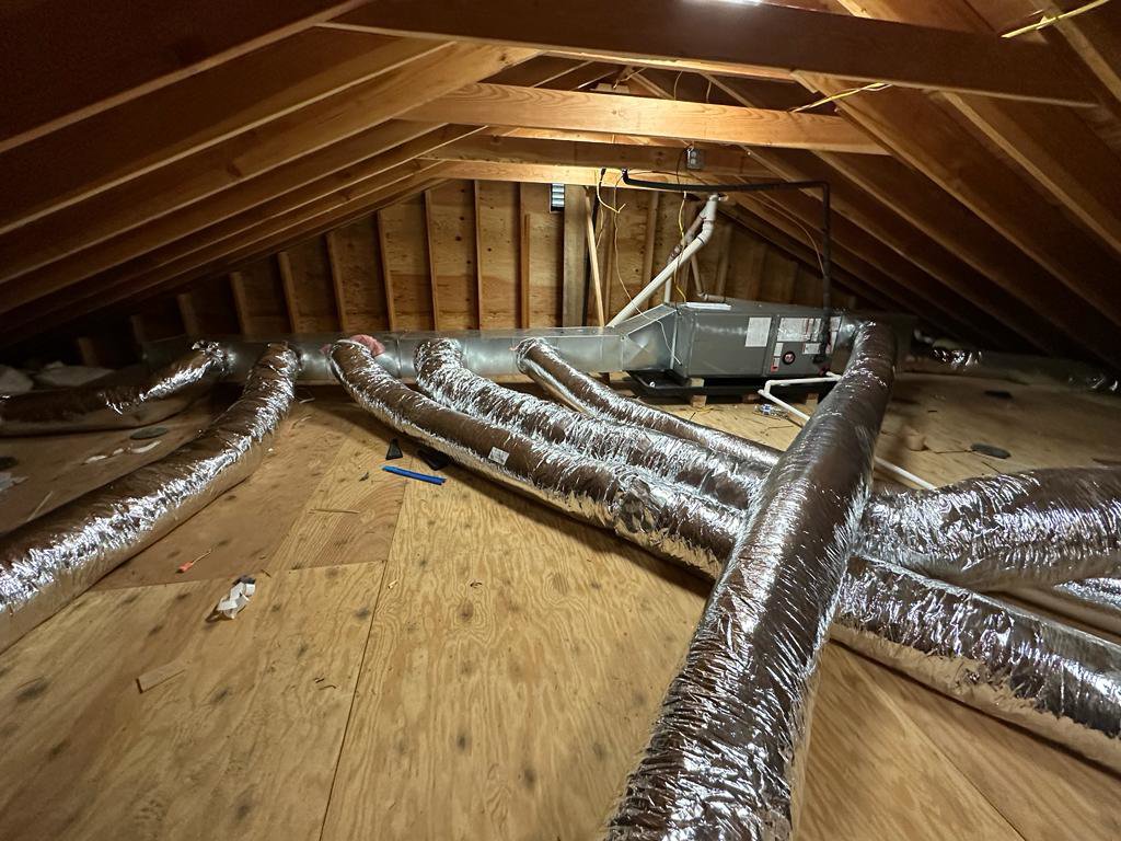 An HVAC air handler unit and extensive ductwork installation visible in an attic, performed by Indoor Expert Heating & Cooling in Paterson, NJ.