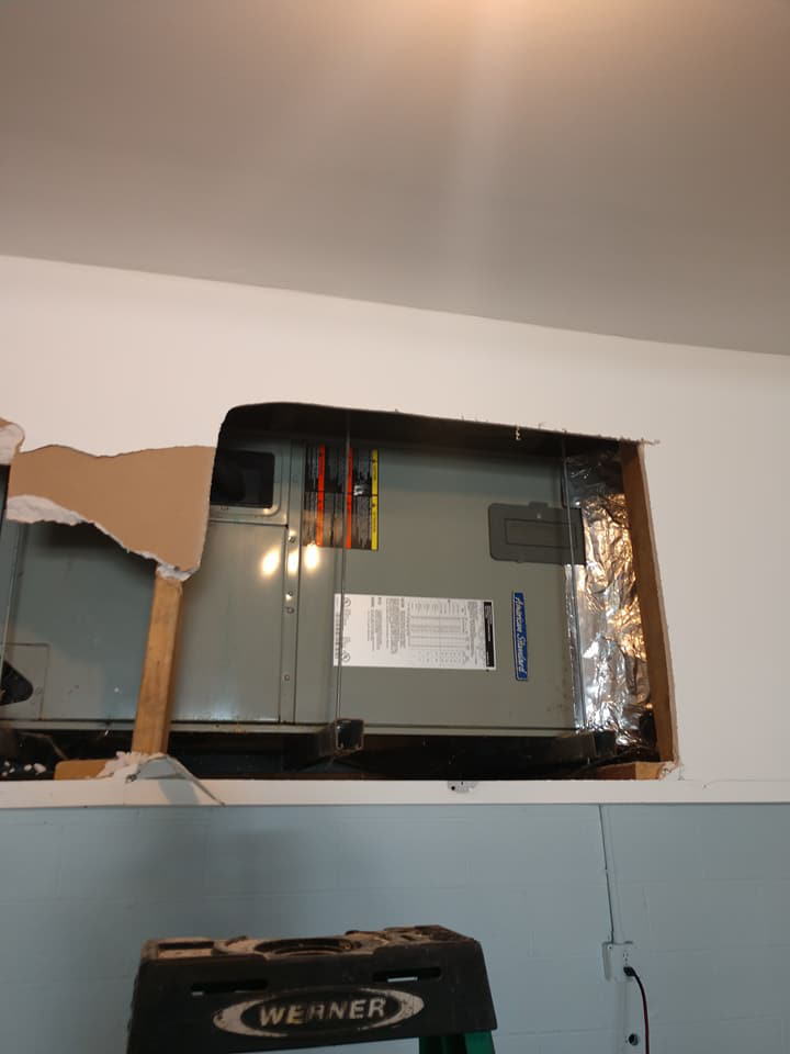 An HVAC air handler unit being serviced through a wall opening by Ryans Ambient Air in Portsmouth, VA.