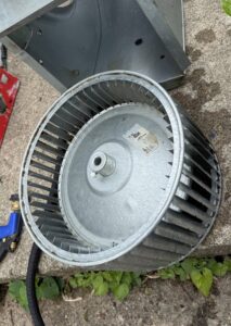 A removed HVAC blower wheel, likely for cleaning or replacement by Allegiance Heating & Air in Greenville, IN.