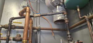 Complex boiler piping system with copper and black pipes, valves, and ductwork by J Hannah Mechanical Inc in Saco, ME.