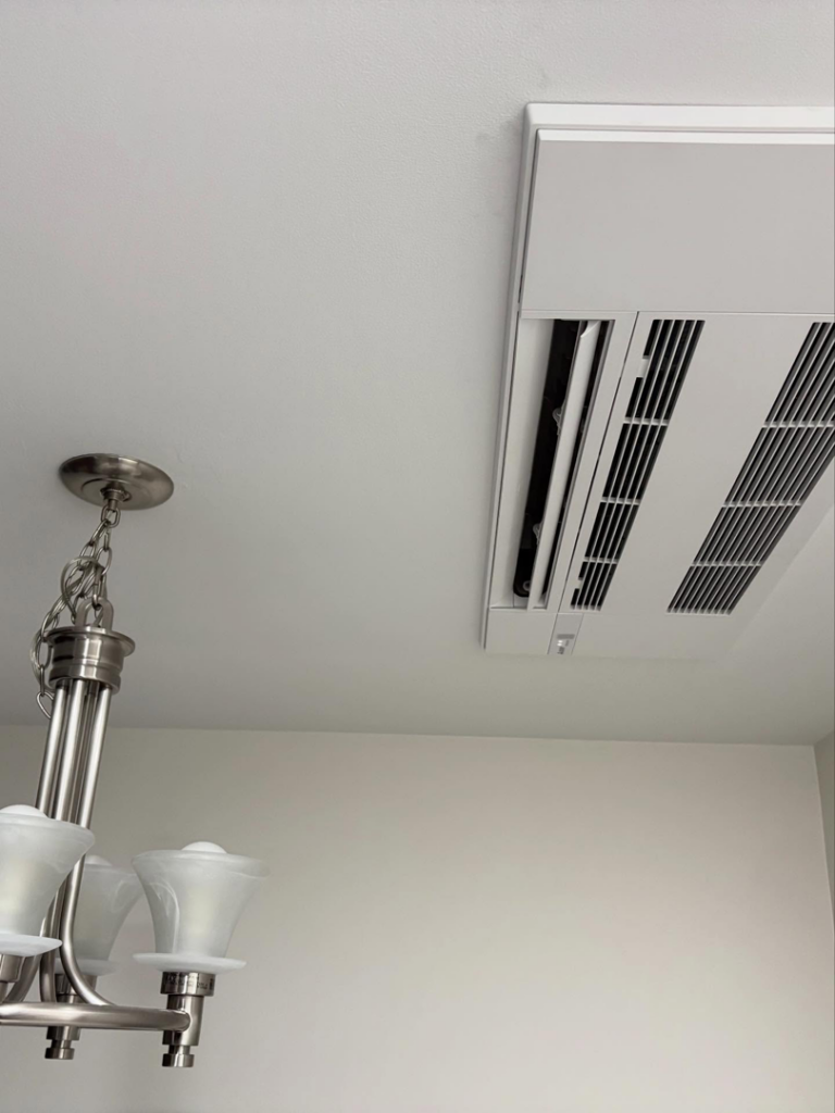 A sleek HVAC ceiling cassette unit installed next to a chandelier in a room by Royal Heating & Air LLC in Sparks, NV