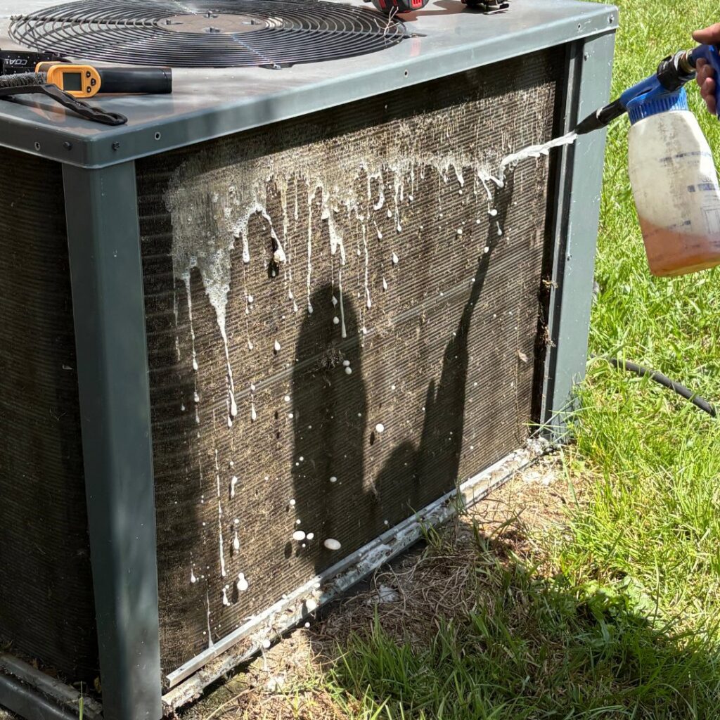 A technician cleaning the outdoor coils of an HVAC unit with a spray bottle during maintenance by T & T HVAC in Amherst, OH.