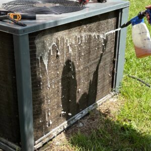A technician cleaning the outdoor coils of an HVAC unit with a spray bottle during maintenance by T & T HVAC in Amherst, OH.