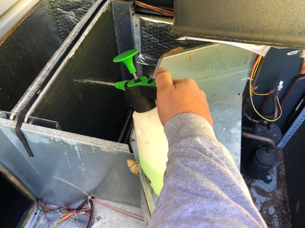 A technician cleaning HVAC coils with a spray bottle during a service call from G&G Heating and Air in Portage, MI.