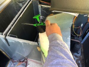 A technician cleaning HVAC coils with a spray bottle during a service call from G&G Heating and Air in Portage, MI.