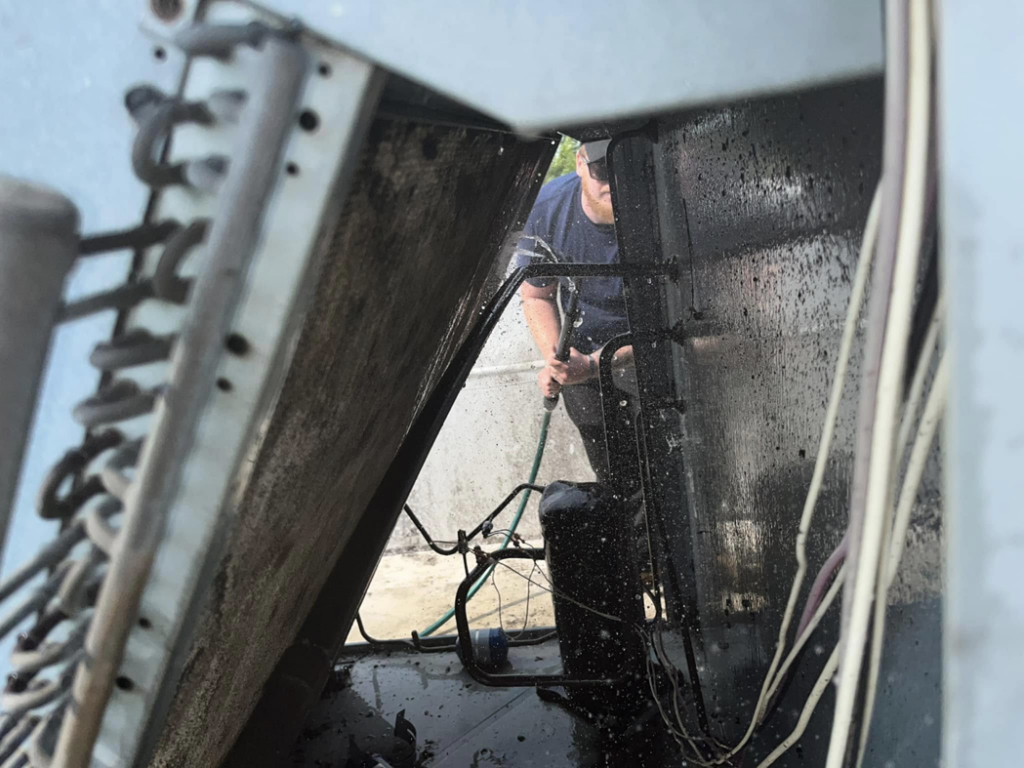 A technician performing HVAC coil cleaning service on an outdoor unit for GrinHouse HVACR in La Grange, KY.