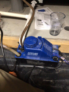 A blue condensate pump on the floor, used in HVAC systems by Waymaker HVAC LLC in Colorado Springs, CO.