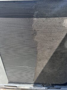 A close-up of an HVAC condenser coil, half cleaned and half dirty, demonstrating a cleaning service by KCC Mechanical, LLC in Sandy, UT.