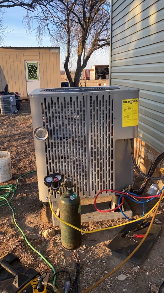 An HVAC technician servicing an outdoor condenser unit with gauges and a refrigerant tank at F & S Williams in Lafayette, IN.