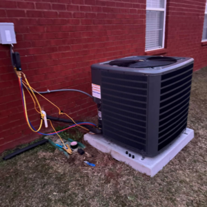 An outdoor HVAC condenser unit being serviced with gauges and hoses by Barnie Sales Heating & A/C in Mobile, AL