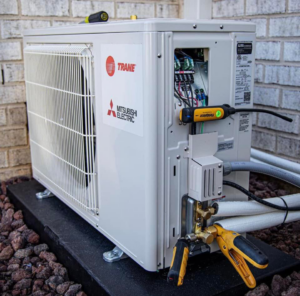 An outdoor HVAC condenser unit with service tools attached, indicating maintenance or repair by ProMasters HVAC Mechanical in New York, NY