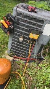 An HVAC technician servicing an outdoor condenser unit with gauges and tools for Affordable heating and air conditioning in Meridian, MS.