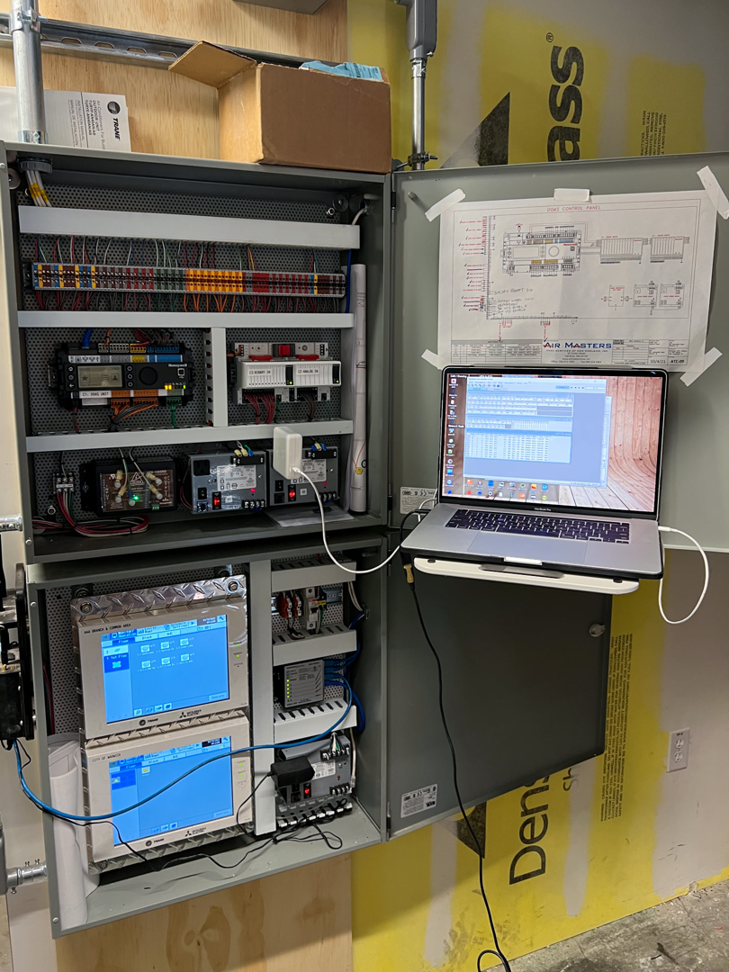 A technician performing diagnostics on an HVAC control panel with a laptop for Air Masters HVAC Services of New England, Inc. in Fall River, MA.