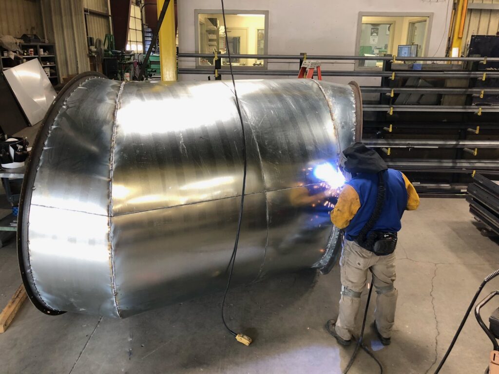A skilled worker welding a large curved HVAC duct component during fabrication at Central Consolidated in Wichita, KS