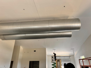 HVAC technician installing large round ducts on a high ceiling by Buck'n Bull HVAC Solutions in Wilmington, NC