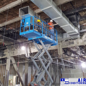 HVAC technicians on a scissor lift installing large air ducts for 1st Team Air Conditioning, Inc. in Anaheim, CA.