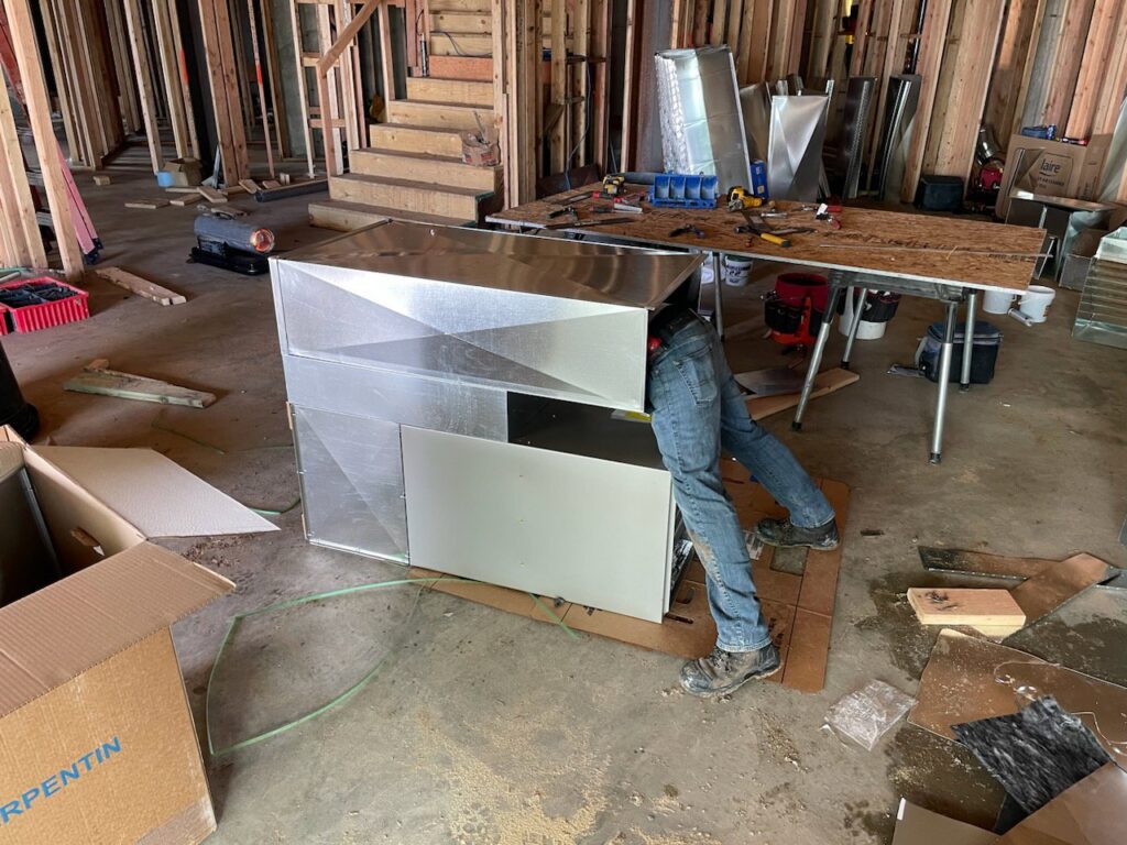 An HVAC technician installing ductwork and an air handler in a new construction home by Authority Heating & Cooling in Orem, UT.