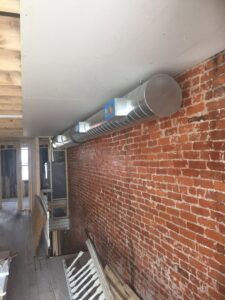 New round metal HVAC ductwork installed along a brick wall during a renovation by Air Done Right in Philadelphia, PA.