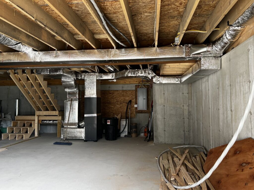 Newly installed and insulated HVAC ductwork running across a basement ceiling by All Points HVAC in Worcester, MA.