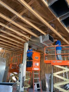 HVAC technicians installing large ductwork on scissor lifts for a commercial project by Dowd Heat & Air in Tulsa, OK.