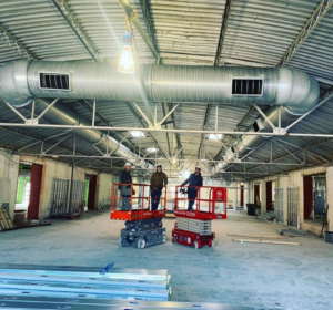 Workers on scissor lifts installing HVAC ductwork in a commercial building for Elemental Air in Sanford, FL.