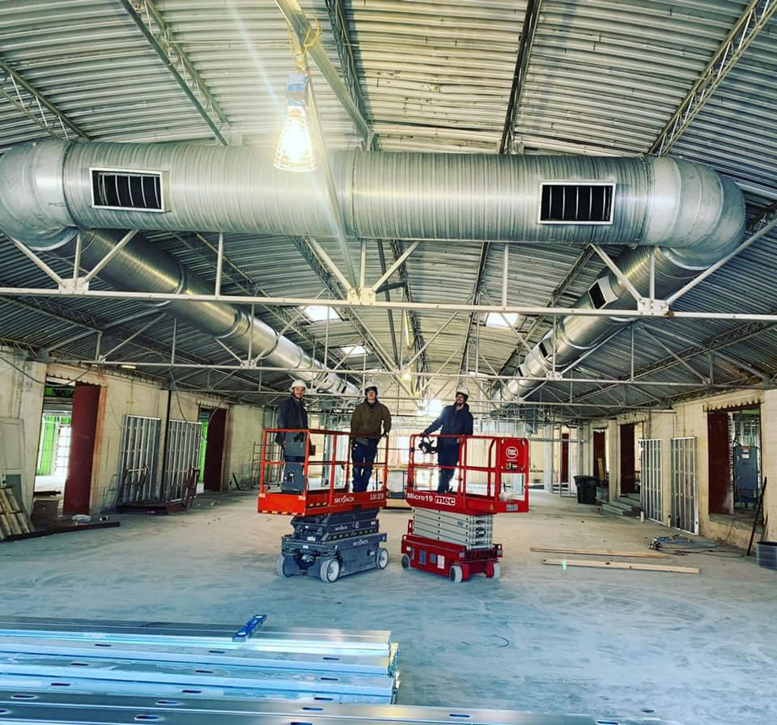Workers on scissor lifts installing HVAC ductwork in a commercial building for Elemental Air in Sanford, FL.