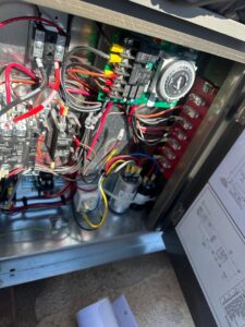 An open HVAC electrical panel showing wiring, capacitors, and circuit board during a repair by Kade Mechanical in Phoenix, AZ.