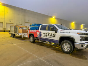 A Texas Air & Heat branded truck towing a trailer with new HVAC equipment for delivery in Arlington, TX.