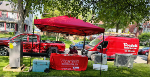 Voegeli Heating & A/C, Inc. displaying various HVAC equipment, including outdoor AC units and a furnace, at an event in Toledo, OH.
