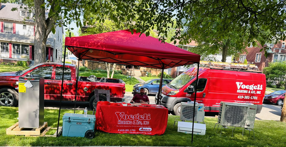 Voegeli Heating & A/C, Inc. displaying various HVAC equipment, including outdoor AC units and a furnace, at an event in Toledo, OH.
