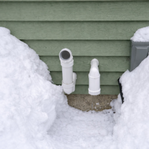 HVAC exhaust and intake pipes on a green house wall surrounded by snow, installed by Black Oak HVAC in Derry, NH