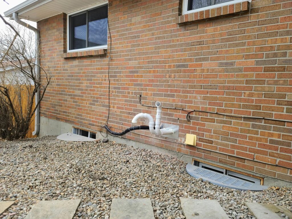 Exterior HVAC venting and piping on a brick residential building, installed by Thin Air Heating and Cooling in Arvada, CO.