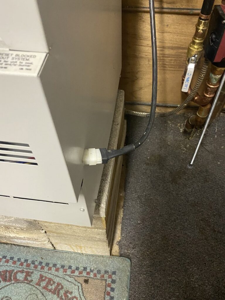 A close-up view of a furnace or boiler component with a power cord and pipes, serviced by Coe Heating & Air Conditioning in Fort Wayne, IN.