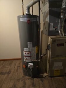 An open furnace unit undergoing repair next to a water heater, demonstrating heating services by 24/7 Heating & Air, LLC in Grand Island, NE.